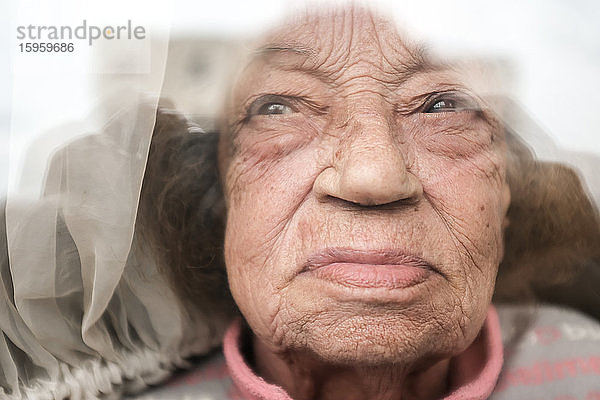 Alte Frau  die während der Coronavirus-Quarantäne durch ein Fenster schaute.