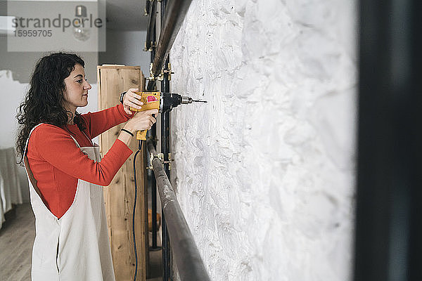 Mittlere erwachsene Frau bohrt Wand in ihrem neuen Laden