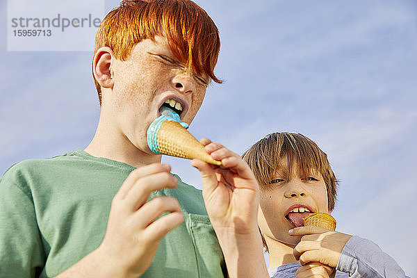 Zwei Jungen stehen im Freien und essen Eistüten.