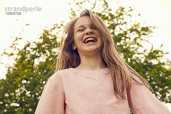 Porträt eines lachenden Mädchens mit langen brünetten Haaren im Freien stehend.