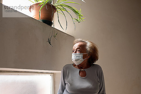 Ältere Frau mit Gesichtsmaske  die während der Corona-Virus-Krise in ihrem Haus stand.