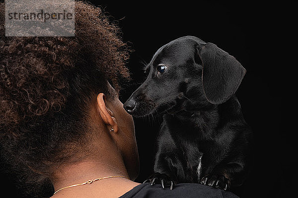 Eine junge Frau mit ihrem Haustier  einem schwarzen Daschund auf der Schulter.