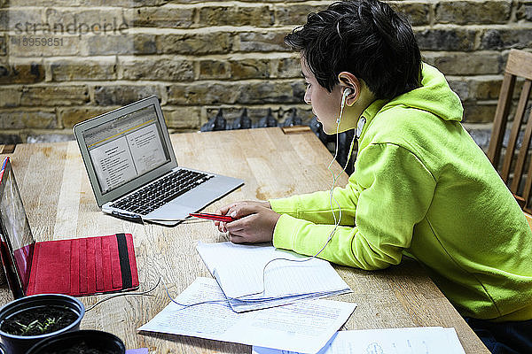 Ein Junge sitzt an einem Schreibtisch und benutzt einen Laptop für eine interaktive Lernsitzung  Hausunterricht  harte Arbeit.
