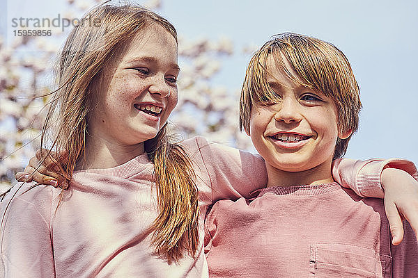 Lächelnder brünetter Junge und Mädchen stehen im Freien  die Arme um die Schultern gelegt.