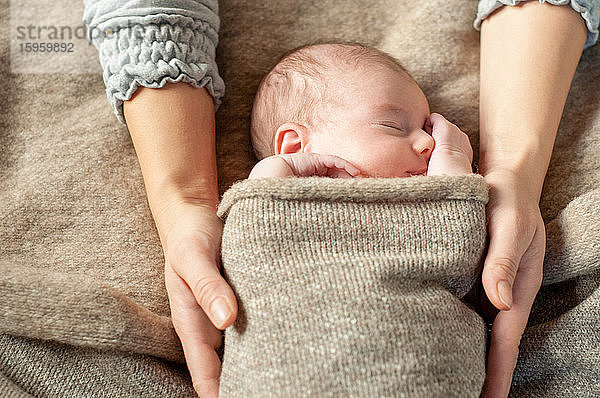 Ein vier Wochen altes Baby wickelte sich in eine braune Decke und wurde von seiner Mutter im Schlaf gehalten.