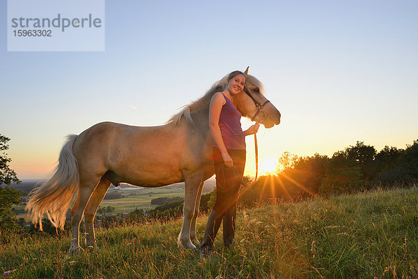 Mädchen mit Pferd auf einer Wiese bei Sonnenuntergang