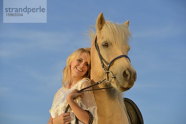 Lächelnde Frau in weißem Kleid mit Pferd unter blauem Himmel