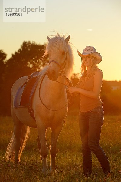 Junge Frau mit Pferd auf einer Wiese im Gegenlicht
