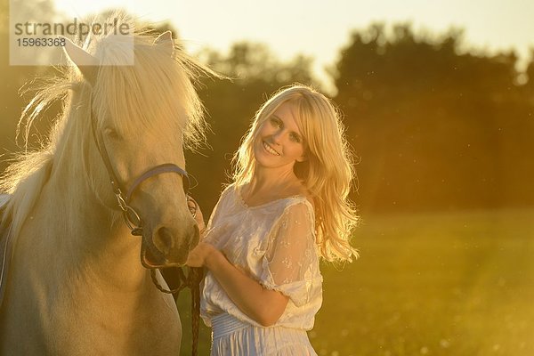 Lächelnde Frau in weißem Kleid mit Pferd auf einer Wiese