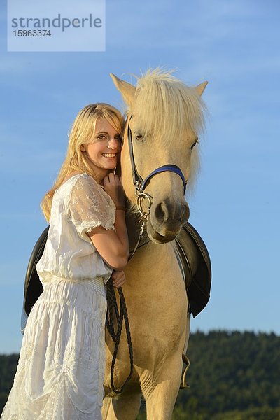 Lächelnde Frau in weißem Kleid mit Pferd unter blauem Himmel