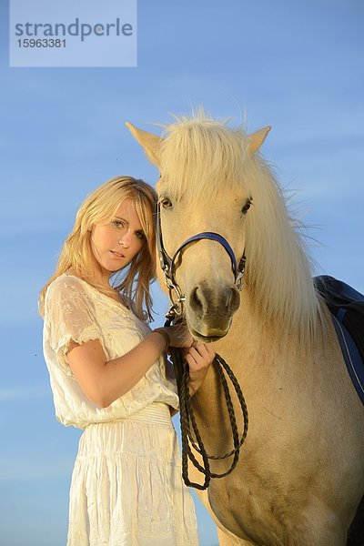 Junge Frau in weißem Kleid mit Pferd unter blauem Himmel