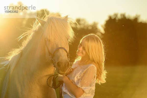 Lächelnde Frau in weißem Kleid mit Pferd auf einer Wiese