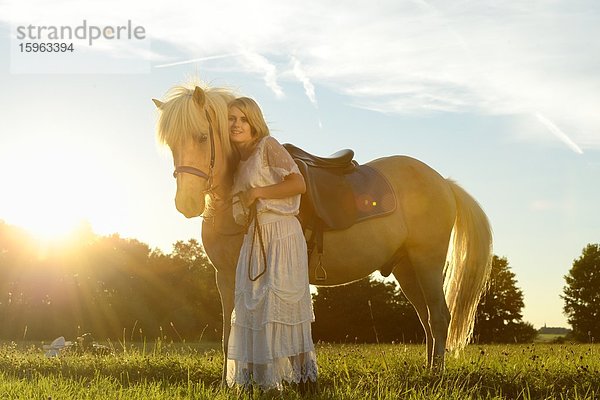 Lächelnde Frau in weißem Kleid mit Pferd auf einer Wiese