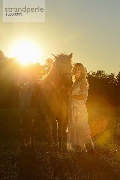 Lächelnde Frau in weißem Kleid mit Pferd auf einer Wiese