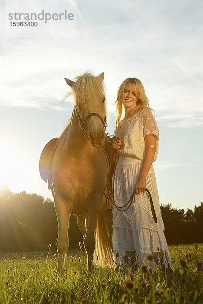 Lächelnde Frau in weißem Kleid mit Pferd auf einer Wiese