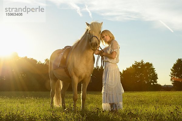 Lächelnde Frau in weißem Kleid mit Pferd auf einer Wiese