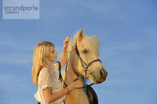 Junge Frau in weißem Kleid mit Pferd unter blauem Himmel