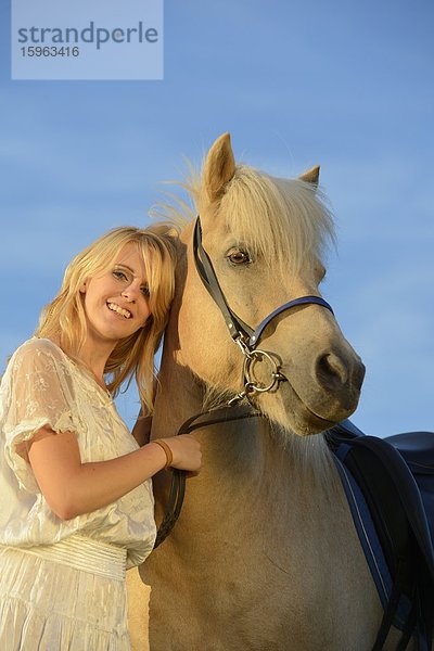 Lächelnde Frau in weißem Kleid mit Pferd unter blauem Himmel