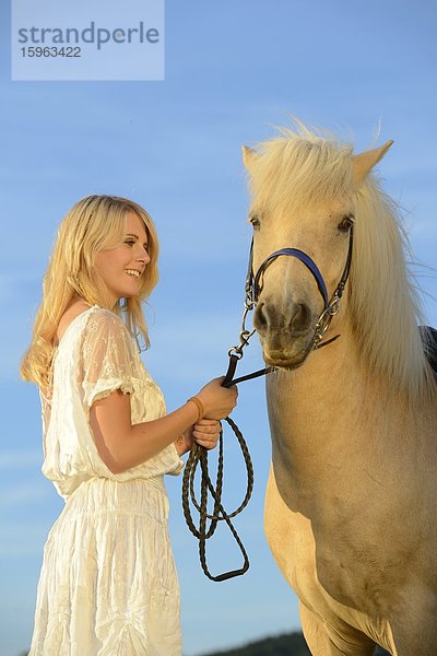 Lächelnde Frau in weißem Kleid mit Pferd unter blauem Himmel