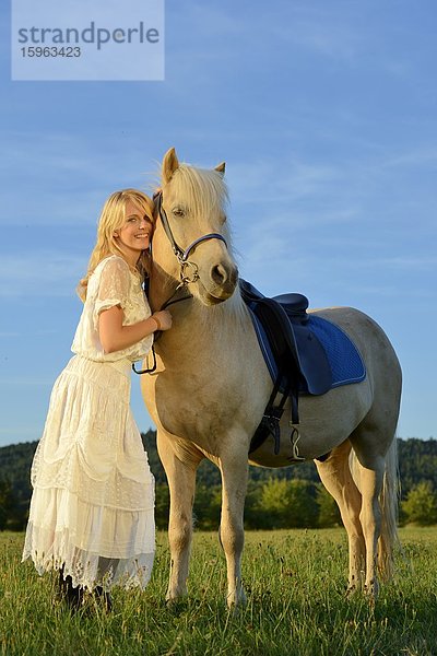 Lächelnde Frau in weißem Kleid mit Pferd auf einer Wiese