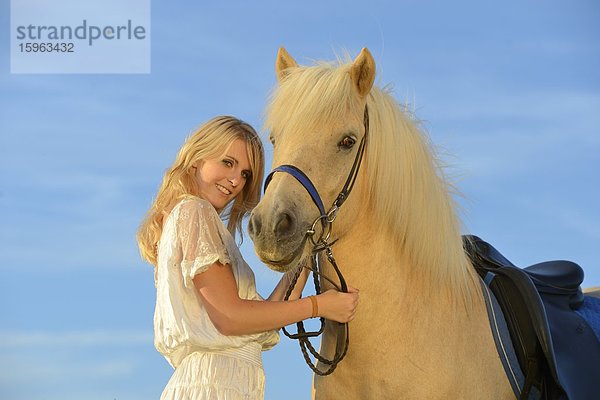 Lächelnde Frau in weißem Kleid mit Pferd unter blauem Himmel