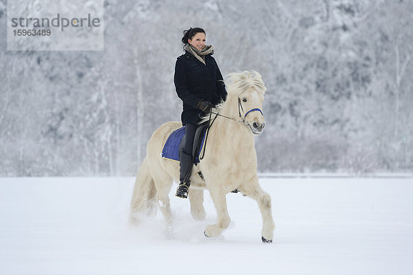 Junge Frau reitet auf Pferd im Schnee