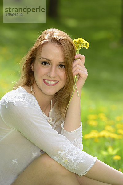 Junge Frau sitzt auf einer Löwenzahn-Wiese im Frühling