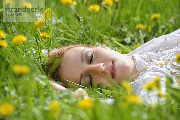 Junge Frau liegt auf einer Löwenzahn-Wiese im Frühling  Portrait