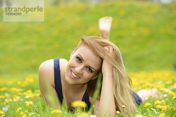 Junge Frau liegt auf einer Löwenzahn-Wiese im Frühling  Portrait