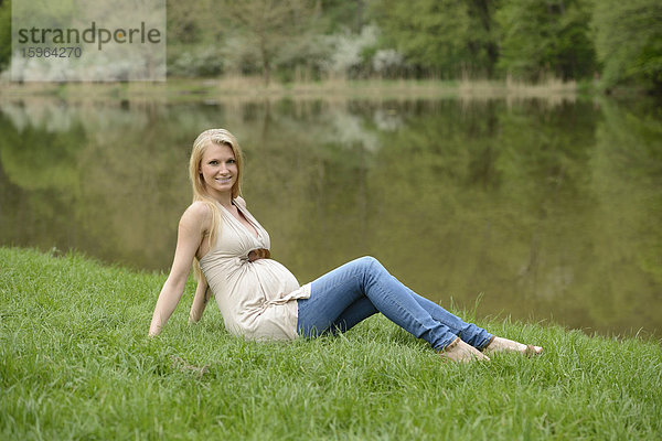 Junge schwangere Frau sitzt auf einer Wiese