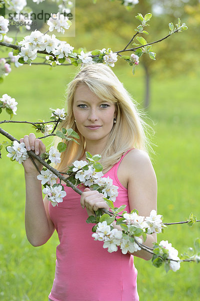 Blonde junge Frau steht neben blühendem Apfelbaum