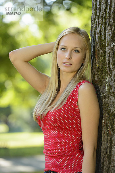 Junge blonde Frau an einem Baumstamm in einem Park