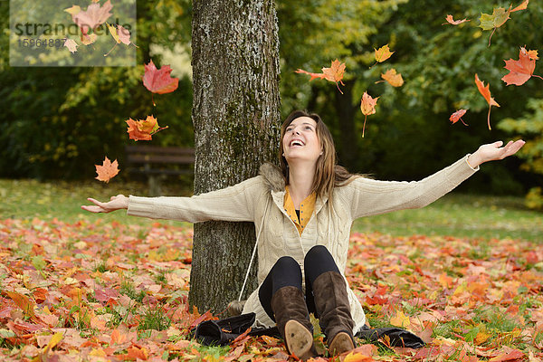Glückliche junge Frau sitzt unter einem Baum im Herbst