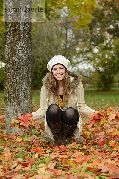 Lächelnde junge Frau an einem Baum im Herbst