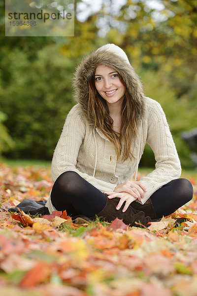 Lächelnde junge Frau sitzt im Herbstlaub