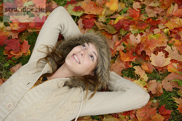Lächelnde junge Frau im Herbstlaub liegend
