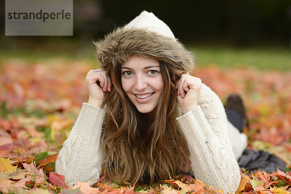 Lächelnde junge Frau im Herbstlaub liegend