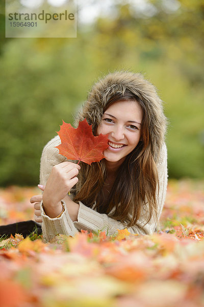 Lächelnde junge Frau im Herbstlaub liegend