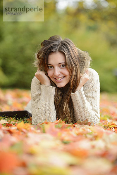 Lächelnde junge Frau im Herbstlaub liegend