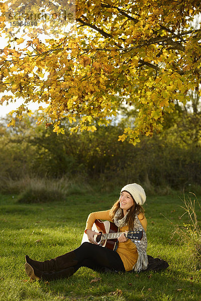Lächelnde junge Frau spielt Gitarre im Herbst