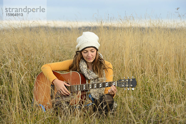 Junge Frau spielt Gitarre auf einem Feld