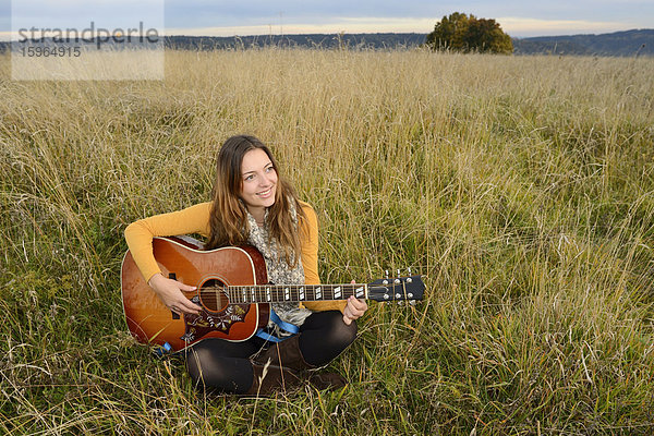 Lächelnde junge Frau spielt Gitarre auf einem Feld