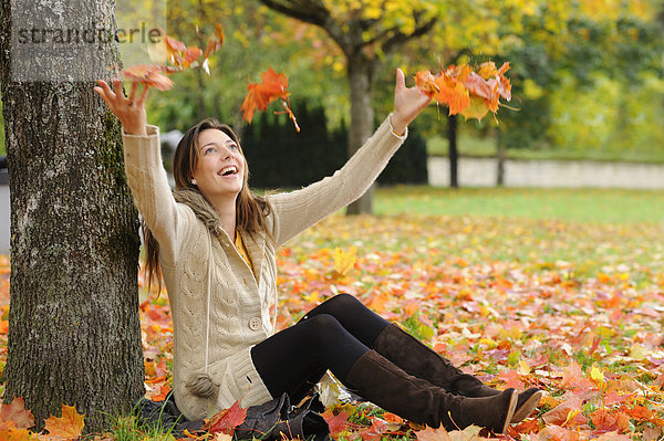 Glückliche junge Frau sitzt unter einem Baum im Herbst