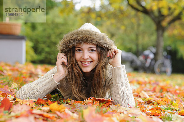 Lächelnde junge Frau im Herbstlaub liegend