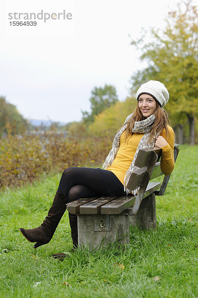 Lächelnde junge Frau sitzt auf einer Bank im Herbst