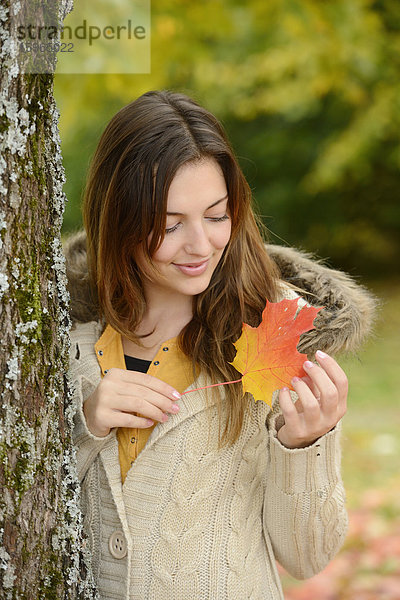 Lächelnde junge Frau mit Herbstblatt