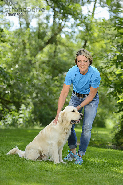 Reife Frau mit einem Golden Retriever im Garten