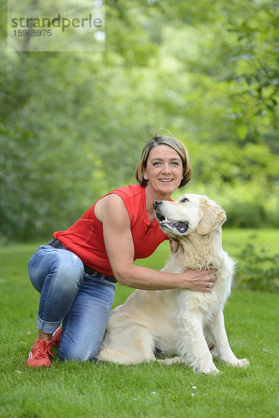 Reife Frau mit einem Golden Retriever im Garten