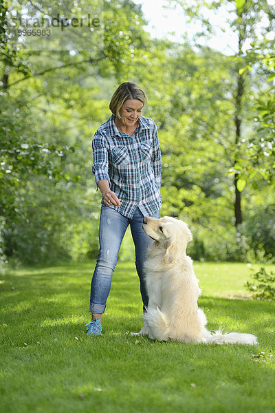 Reife Frau mit einem Golden Retriever im Garten