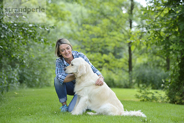 Reife Frau mit einem Golden Retriever im Garten